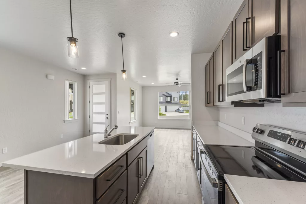 Modern kitchen with dark wood cabinets, white countertops, stainless steel appliances, and pendant lighting.