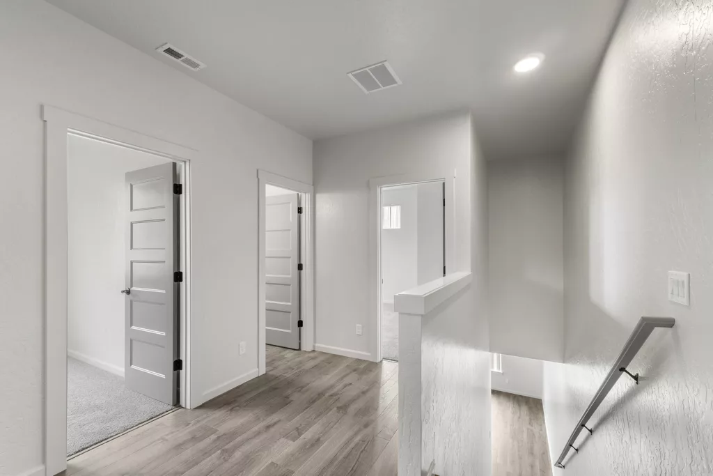 A bright, minimalistic hallway with light wood flooring, white walls, and multiple white doors.