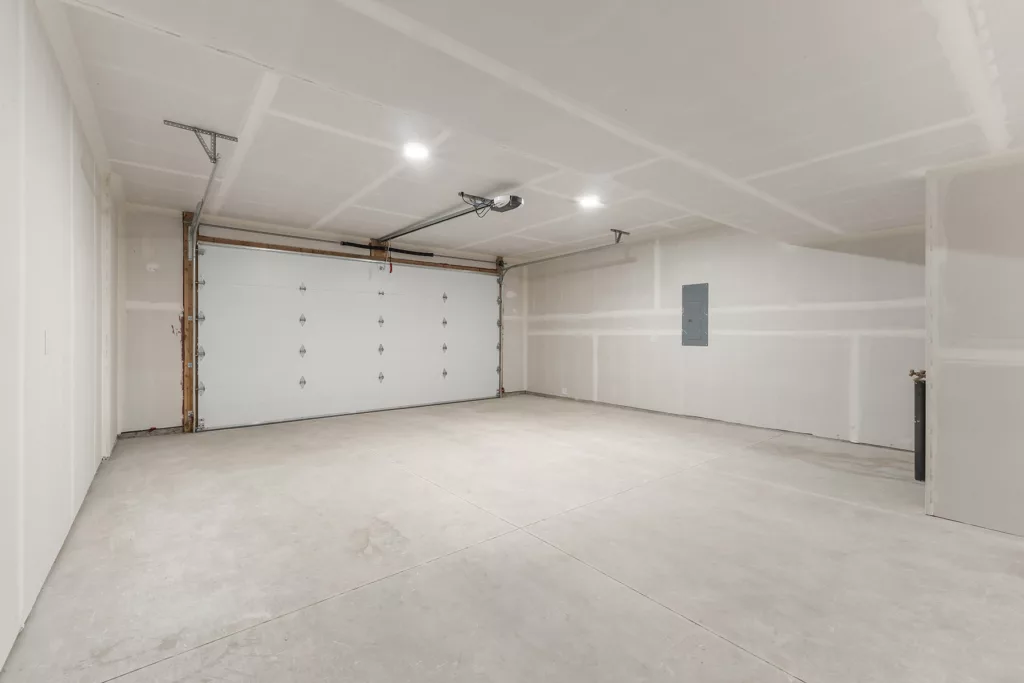 An empty garage with white drywall, a closed white garage door, and a ceiling-mounted garage door opener.