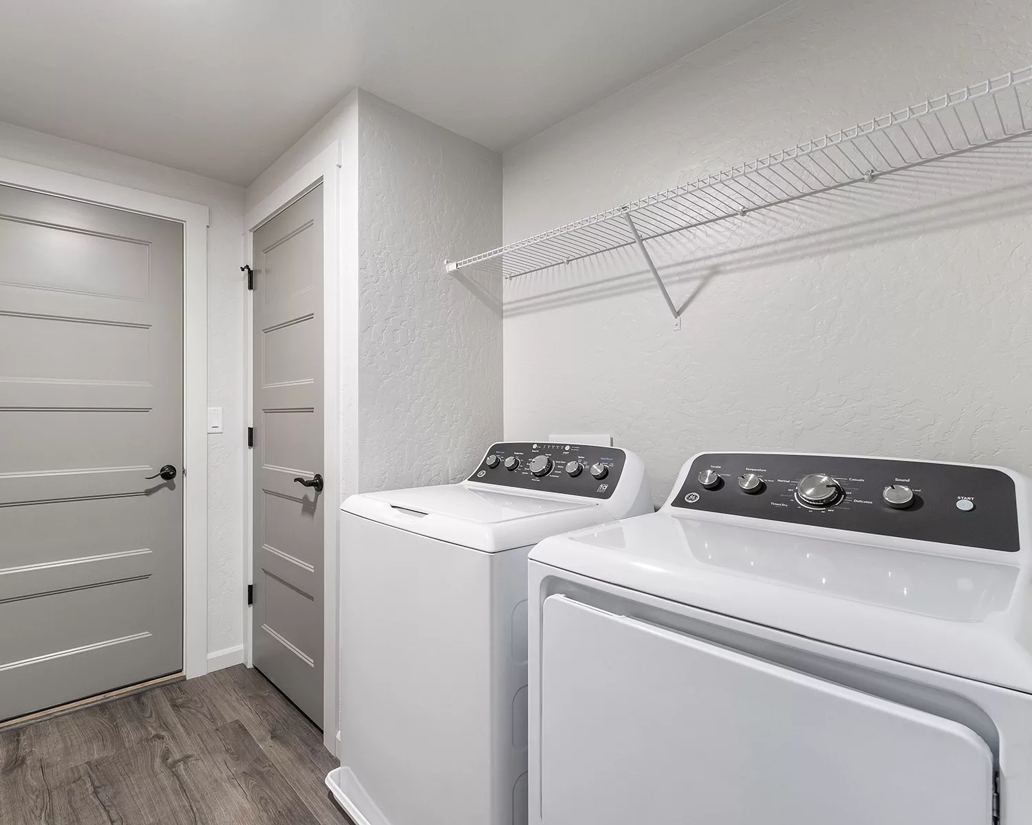 Laundry room with a washer and dryer, gray doors, and a white wire shelf above.