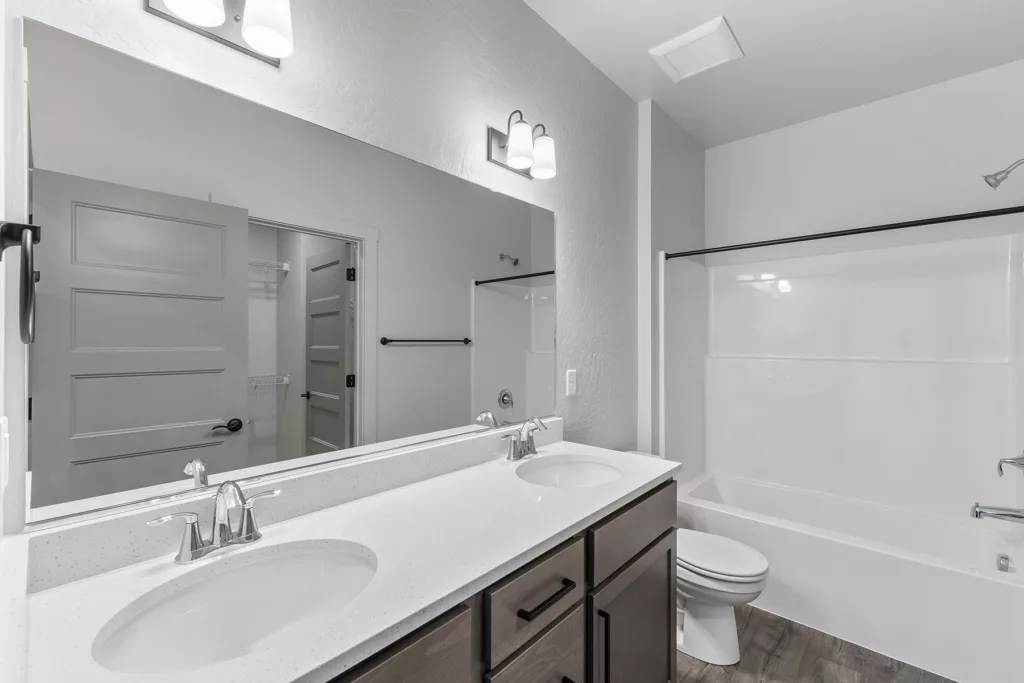 A modern bathroom with a double sink vanity, a large mirror, and a bathtub with a shower behind a partial wall.