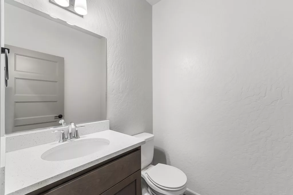A modern bathroom with a wooden vanity, white countertop, sink, toilet, and a wall-mounted mirror.
