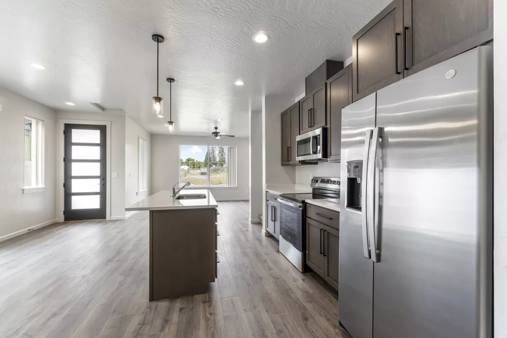 Modern kitchen with stainless steel appliances, dark wood cabinets, and a center island, next to a bright dining area.