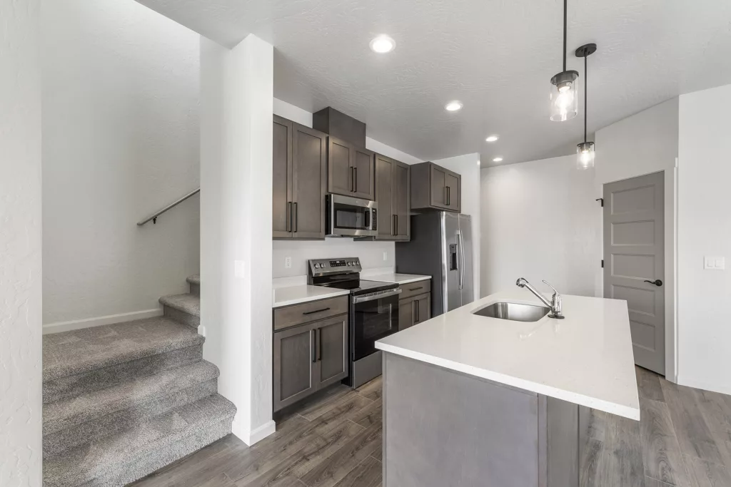A modern kitchen with dark cabinets, a stainless steel stove, and a refrigerator next to a central island with a sink.