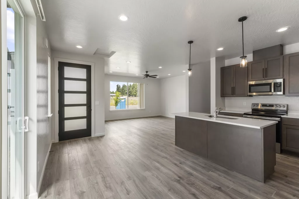 A modern open-plan kitchen and living area with dark wood cabinets, stainless steel appliances, and large windows.