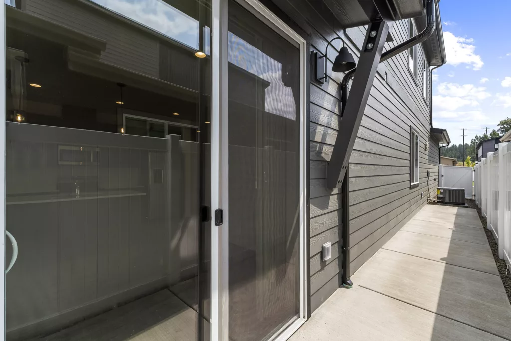 Sliding glass door on a patio with a view of a modern home's exterior, surrounded by a fenced area.