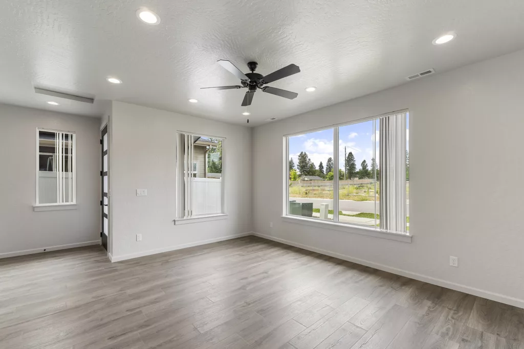 An empty room with wood flooring, large windows, a ceiling fan, recessed lighting, and neutral-colored walls.
