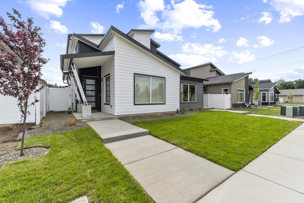 Modern house with white siding, large windows, and a sloped roof, surrounded by a neatly manicured lawn and paved pathway.