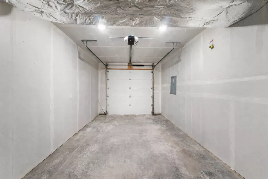 Empty garage interior with a closed white garage door, concrete floor, and unpainted drywall walls and ceiling.
